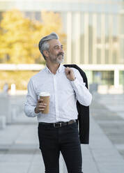 Smiling businessman holding blazer and disposable cup - JCCMF04389