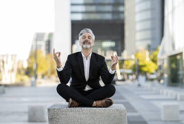 Businessman meditating sitting cross-legged on seat - JCCMF04400