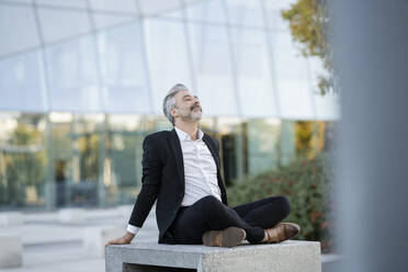 Businessman sitting cross-legged relaxing on seat - JCCMF04401