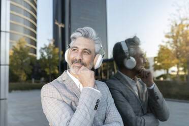 Thoughtful businessman listening music on headphones - JCCMF04418