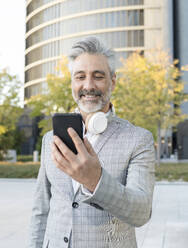 Businessman with headphones using smart phone - JCCMF04419