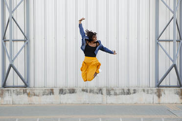 Carefree woman jumping in front of wall - DMGF00630