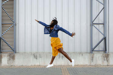 Cheerful woman jumping in front of wall - DMGF00637