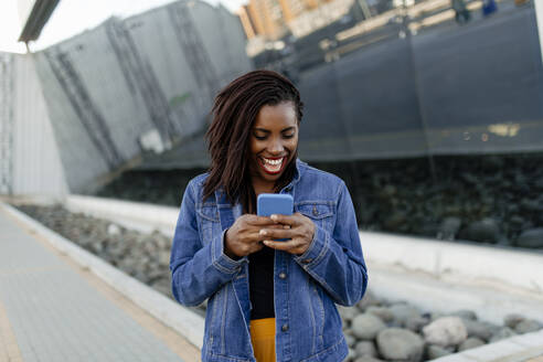 Happy woman in denim jacket using smart phone - DMGF00644