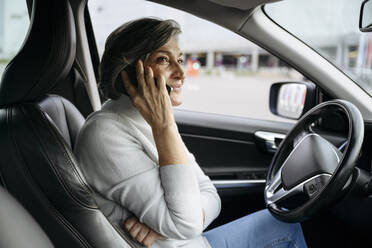 Frau, die im Auto sitzend mit ihrem Smartphone telefoniert - VYF00664