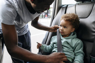 Lächelnder Vater stellt den Sicherheitsgurt seiner Tochter im Auto ein - VYF00668