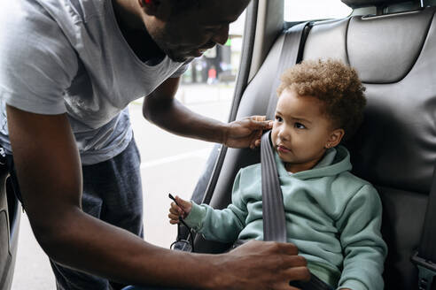 Lächelnder Vater stellt den Sicherheitsgurt seiner Tochter im Auto ein - VYF00668