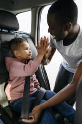 Vater gibt seinem Sohn beim Anschnallen im Auto ein High-Five - VYF00669