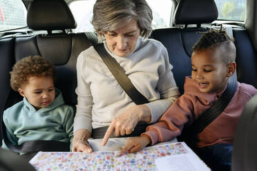 Großmutter liest mit Enkelkindern im Auto ein Buch - VYF00672