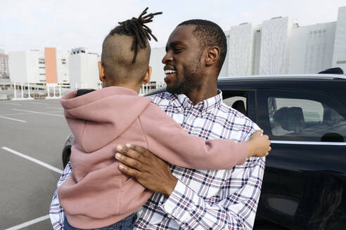 Lächelnder Vater mit Sohn auf dem Arm auf einem Parkplatz - VYF00675