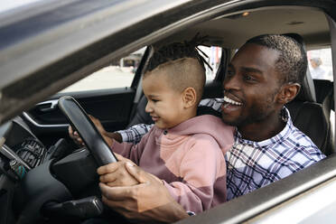 Happy father and son playing with steering wheel in car - VYF00678