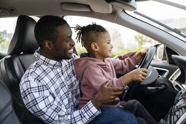Smiling father and son playing with steering wheel in car - VYF00681