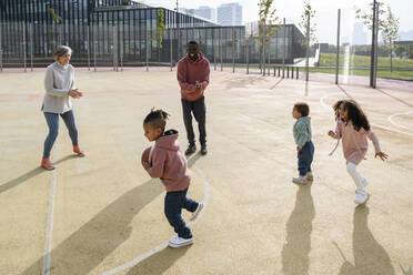 Lächelnde Familie spielt mit Basketball auf einem Sportplatz - VYF00693