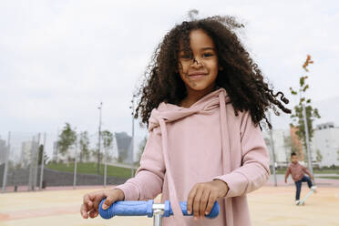 Lächelndes Mädchen mit Tretroller auf dem Sportplatz - VYF00720