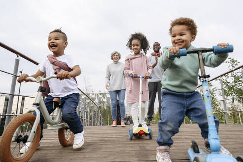 Fröhliche Kinder spielen mit Roller und Fahrrad auf einer Brücke - VYF00734