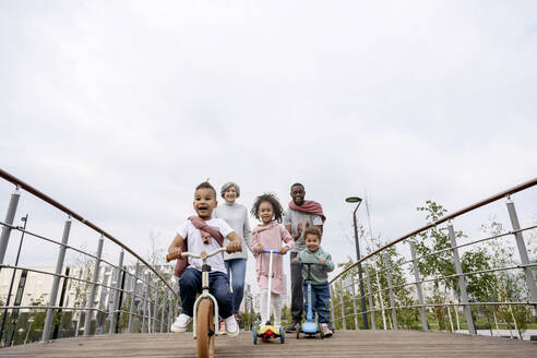 Children riding push scooter and bicycle on bridge - VYF00735