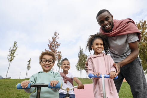 Smiling father standing with playful children at park - VYF00738