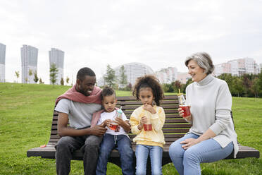 Vater schaut Kindern beim Trinken auf einer Parkbank zu - VYF00746