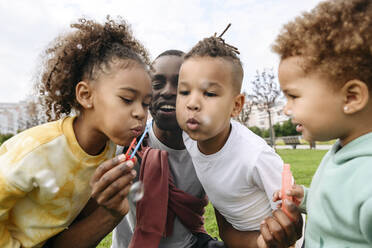 Children blowing bubble with father in park - VYF00751