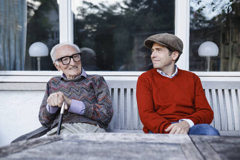 Smiling man wearing beret looking at father on bench - AANF00160