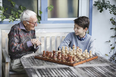 Smiling boy playing chess with grandfather in backyard - AANF00170