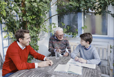 Smiling man looking at son and father talking over turbine model in backyard - AANF00173