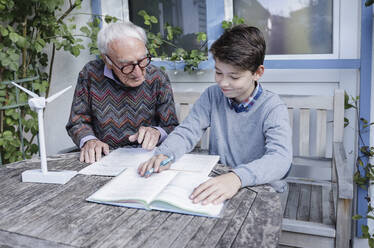 Senior man assisting grandson studying at table - AANF00175