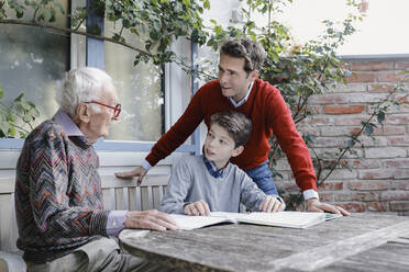 Smiling man and boy looking at senior father talking in backyard - AANF00176