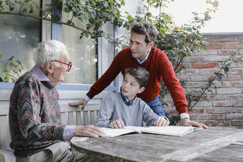 Lächelnder Mann und Junge schauen auf älteren Vater, der im Hinterhof spricht - AANF00176