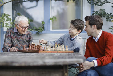 Man looking at father playing chess with son in backyard - AANF00179