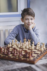 Lächelnder Junge mit Hand am Kinn vor einem Schachbrett - AANF00181