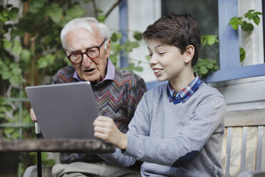 Smiling boy showing laptop to grandfather in backyard - AANF00183