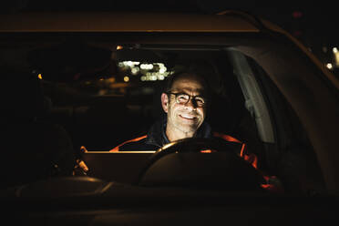 Lächelnder Ingenieur mit Laptop im Auto bei Nacht - UUF24995