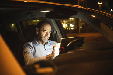 Businessman using laptop in car at night - UUF25000