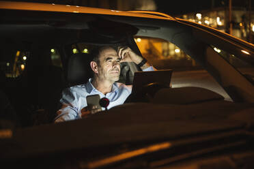 Thoughtful businessman with mobile phone and laptop in car - UUF25004