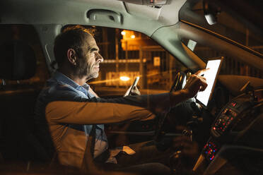 Businessman using tablet PC in car at night - UUF25006