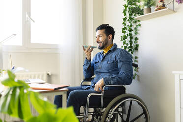 Behinderter männlicher Freiberufler, der zu Hause mit seinem Smartphone telefoniert - JCCMF04431