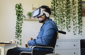 Lächelnder behinderter Geschäftsmann benutzt Virtual-Reality-Headset zu Hause - JCCMF04434