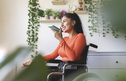 Smiling disabled woman talking on mobile phone at home - JCCMF04449