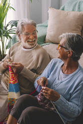 Smiling couple knitting wool together at home - SIPF02654