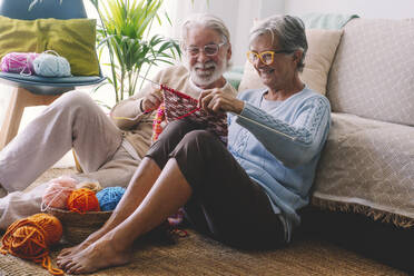 Smiling senior couple knitting wool together in living room - SIPF02656