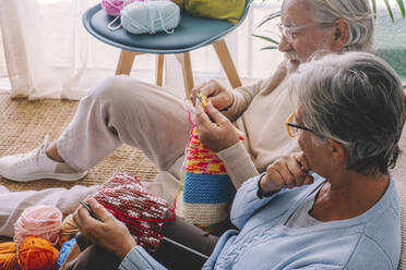 Woman looking at man knitting wool at home - SIPF02657