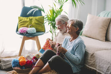 Smiling senior couple knitting wool together at home - SIPF02662