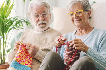 Senior man looking at woman knitting wool at home - SIPF02663