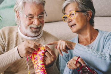 Woman teaching man knitting wool with needle at home - SIPF02666