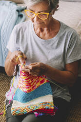 Senior woman knitting wool with needle in living room - SIPF02675