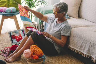 Woman with laptop checking knitted wool at home - SIPF02679