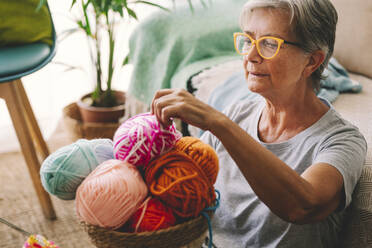 Woman choosing ball of wool from basket at home - SIPF02682