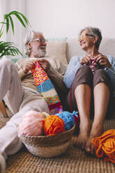 Lächelndes älteres Paar strickt Wolle im Wohnzimmer - SIPF02686