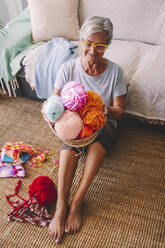 Woman with basket of wool balls sitting in living room - SIPF02693